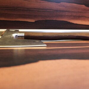 May include: A silver axe with a wooden handle. The axe is lying on a dark brown wooden surface.