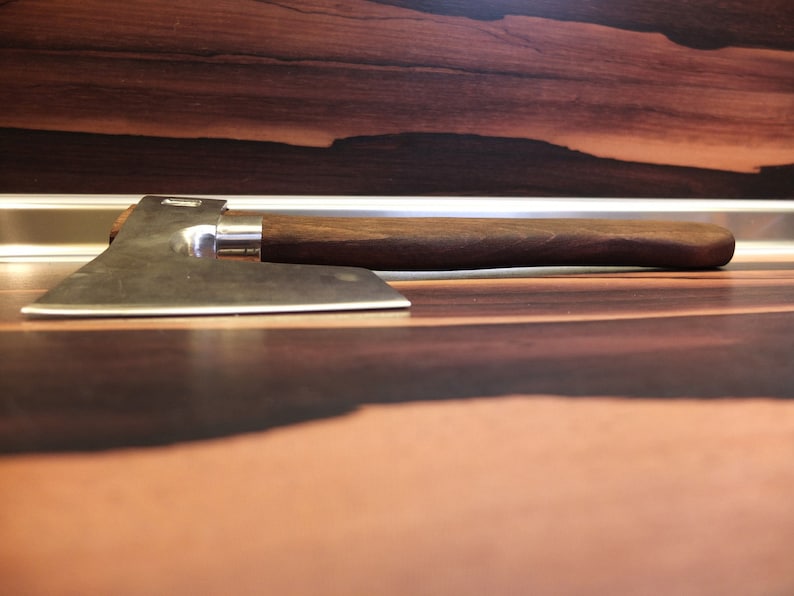 May include: A silver axe with a wooden handle. The axe is lying on a dark brown wooden surface.