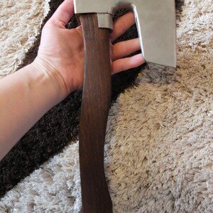 May include: A hand holds a small, silver axe with a dark brown wooden handle. The axe has a curved blade and a rounded head.