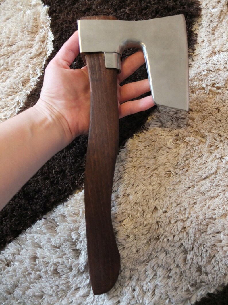 May include: A hand holds a small, silver axe with a dark brown wooden handle. The axe has a curved blade and a rounded head.