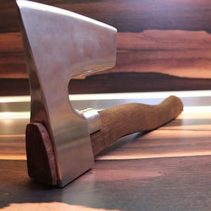 May include: A silver axe with a wooden handle. The axe is lying on a wooden surface.