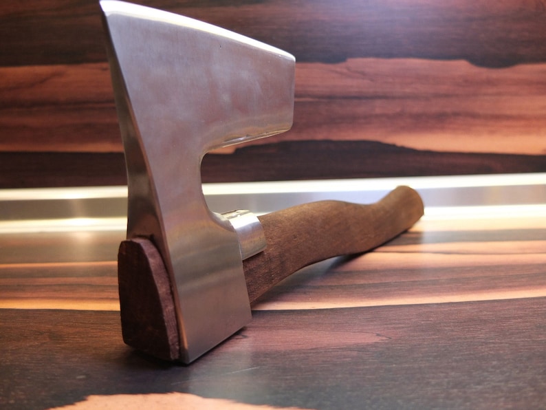 May include: A silver axe with a wooden handle. The axe is lying on a wooden surface.
