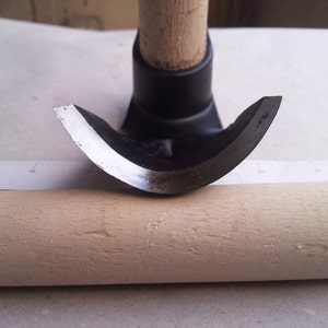 Peut inclure: Gros plan d'un outil de travail du bois incurvé avec une poignée noire et une lame argentée tranchante. L'outil repose sur une surface en bois.