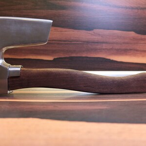 May include: A silver axe with a wooden handle. The axe has a curved blade and a rounded handle.