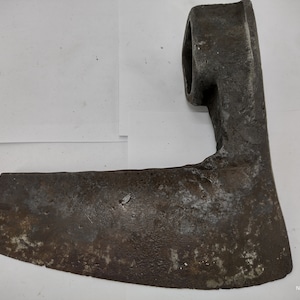 May include: A rusty, metal axe head with a curved blade and a round hole at the top for attaching a handle.