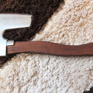 May include: A small, hand-forged axe with a brown wooden handle. The axe head is made of polished metal and has a slight curve to the blade.