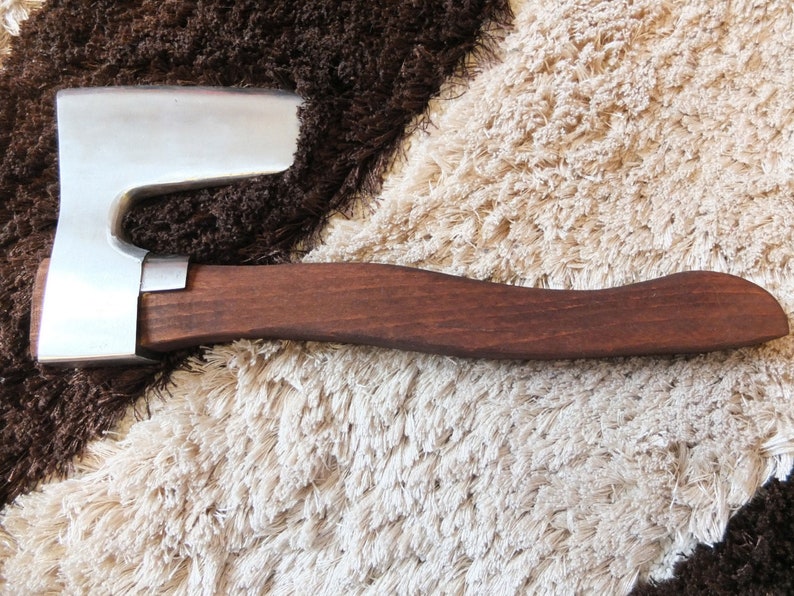 May include: A small, hand-forged axe with a brown wooden handle. The axe head is made of polished metal and has a slight curve to the blade.