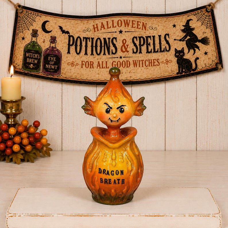 May include: A ceramic potion bottle featuring a yellow and orange gradient finish with a sculpted lid shaped like a mischievous creature with pointed ears and fangs. The front of the bottle is labeled with the black text Dragon Breath.