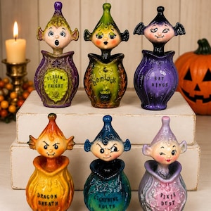 May include: A set of six decorative potion bottles with sculpted character stoppers. Each bottle features a unique color and label: Scream of Fright, Hemlock, Bat Wings, Dragon Breath, Lightning Bolts, and Pixie Dust. The figures have distinct facial expressions and head shapes.
