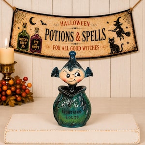 May include: A ceramic jar with a lid shaped like a mischievous imp with bat-like ears. The jar is teal and green with a glossy finish, featuring the text "LIGHTNING BOLTS" on the front. The lid is a dark blue, pointed figure with a smirk.