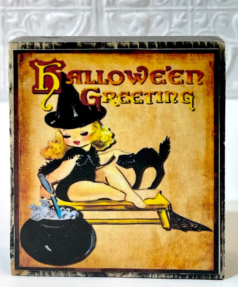 May include: A vintage Halloween greeting card featuring a witch with a black hat and a black cat. The witch is stirring a cauldron with a wooden spoon. The card has a yellowed background with the text "Halloween Greeting" in red and black lettering.