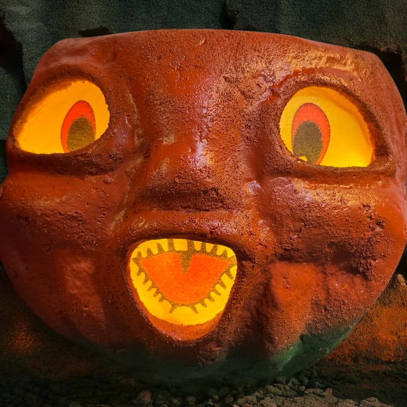 May include: A large, orange, carved pumpkin with glowing yellow eyes and mouth. The pumpkin has a textured surface and a friendly, cartoonish expression. The interior of the eyes and mouth glow with a warm, inviting light, suggesting a Halloween theme.