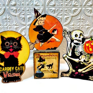 May include: Four vintage Halloween decorations: a black cat with a red bow tie, a witch flying on a broomstick, a skeleton holding a pumpkin, and a wooden block with a witch and the text "Halloween Greeting".