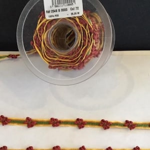 May include: A spool of gold and burgundy trim with small flower-shaped embellishments. The trim is 25 meters long and made of 100% polyester.