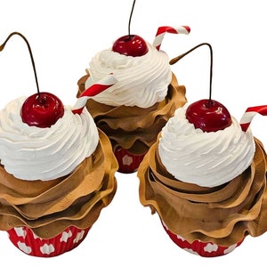 May include: Three chocolate cupcakes with white frosting and red cherries on top. Each cupcake has a red and white striped straw sticking out of the frosting.