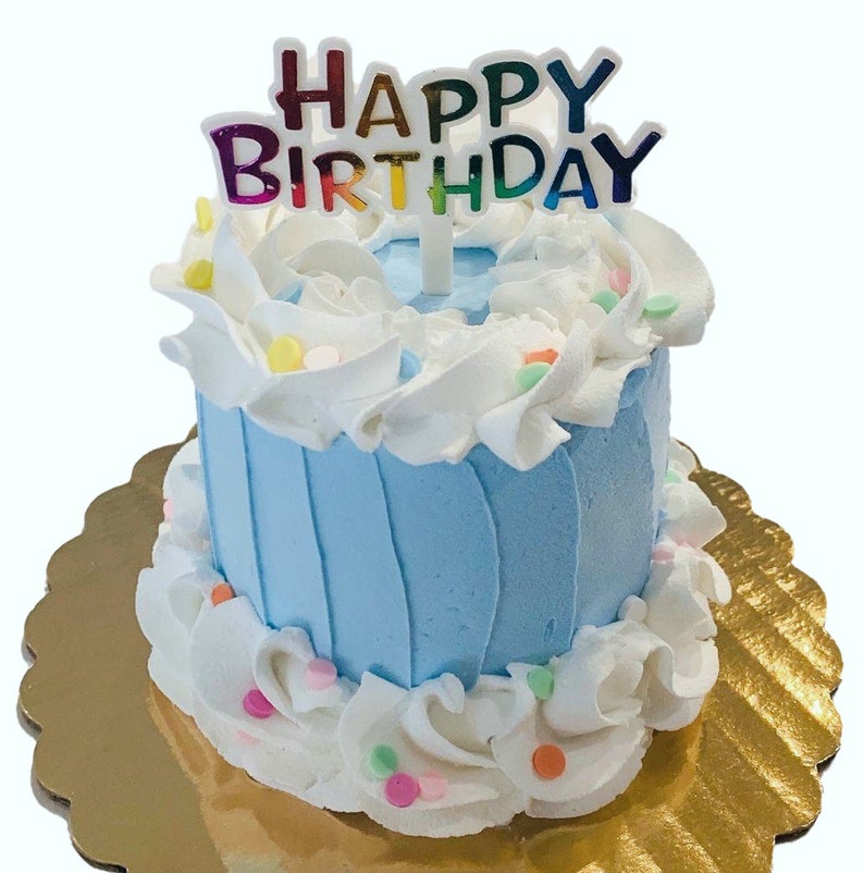 Pu&ograve; includere: Una piccola torta di compleanno blu e bianca con un topper "Buon compleanno". La torta &egrave; decorata con glassa bianca e codette colorate.