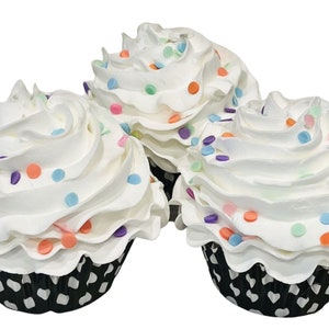 May include: Three white cupcakes with white frosting and colorful sprinkles. The cupcakes are in black and white paper liners.