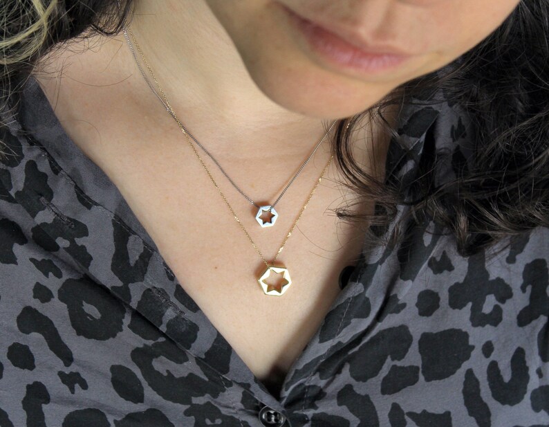 May include: Two silver necklaces with star-shaped pendants. The top necklace has a smaller star pendant, while the bottom necklace has a larger star pendant.