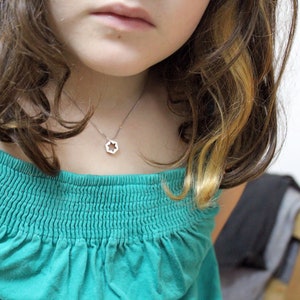 May include: A young person wearing a teal blue off-the-shoulder shirt with a silver star-shaped pendant necklace.
