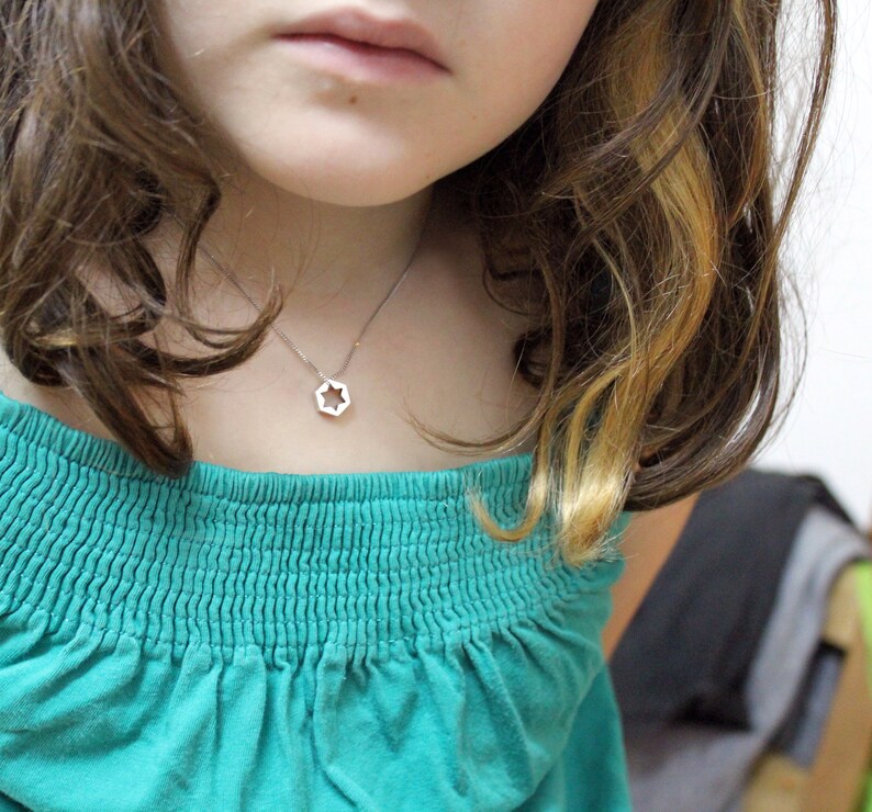 May include: A young person wearing a teal blue off-the-shoulder shirt with a silver star-shaped pendant necklace.