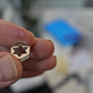 May include: A silver-toned metal charm shaped like a six-pointed star with a cutout in the center.