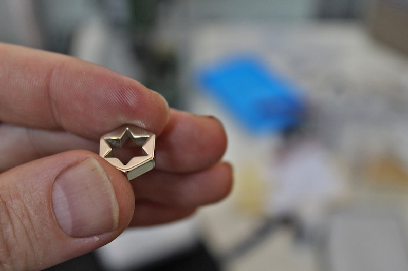 May include: A silver-toned metal charm shaped like a six-pointed star with a cutout in the center.