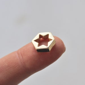 May include: A gold-colored metal charm shaped like a hexagon with a six-pointed star cut out in the center.