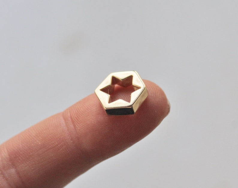 May include: A gold-colored metal charm shaped like a hexagon with a six-pointed star cut out in the center.