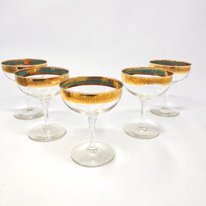 Könnte beinhalten: Fünf klare Champagner-Coupe-Gläser mit goldenen Rändern und türkisfarbenen Akzenten. Die Gläser haben ein klassisches Design mit einer runden Schale und einem schlanken Stiel. Der goldene Rand hat ein dekoratives Muster.