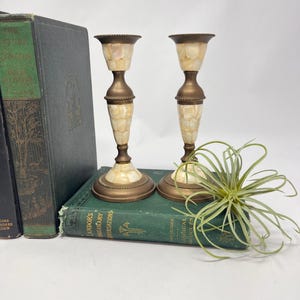 Pode incluir: Dois castiçais vintage de latão e madrepérola. Os castiçais têm um design canelado e estão colocados em um livro verde. Os castiçais têm aproximadamente 20 cm de altura.