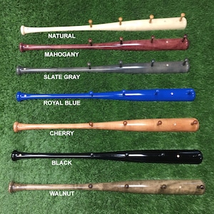 May include: Seven wooden baseball bat coat racks in different colors, including natural, mahogany, slate gray, royal blue, cherry, black, and walnut. Each bat has five wooden pegs for hanging items.