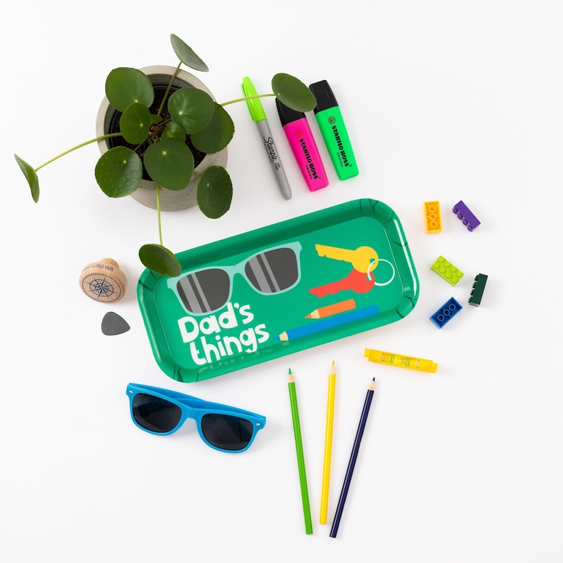 K&ouml;nnte beinhalten: Gr&uuml;nes Tablett mit dem Text "Dad's things" und einer Sonnenbrille, einem Schl&uuml;ssel und Bleistiften. Au&szlig;erdem gibt es bunte Bausteine und Textmarker.