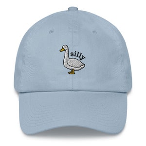 May include: A light blue baseball cap with an embroidered white duck and the word "silly" in black text.