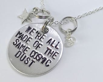 May include: A silver necklace with a charm that reads "We're all made of the same cosmic dust". The necklace also has a small star charm and a bead charm.