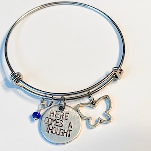 May include: Silver expandable bracelet with a charm that says "Here comes a thought" and a butterfly charm. The bracelet also has a small blue bead.