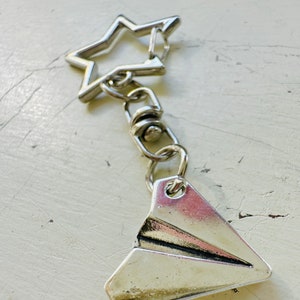 May include: Silver keychain with a paper airplane charm and a star-shaped ring.