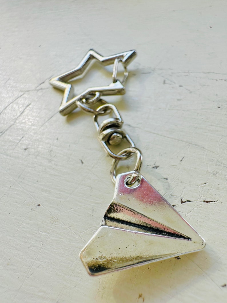 May include: Silver keychain with a paper airplane charm and a star-shaped ring.