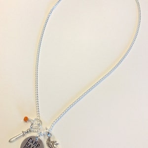 Pode incluir: Um colar de prata com um pingente que diz "Camp Half Blood" e que apresenta um cavalo alado, uma espada e uma conta laranja.