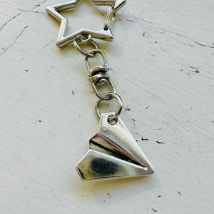May include: Silver keychain with a star-shaped charm and a paper airplane charm.