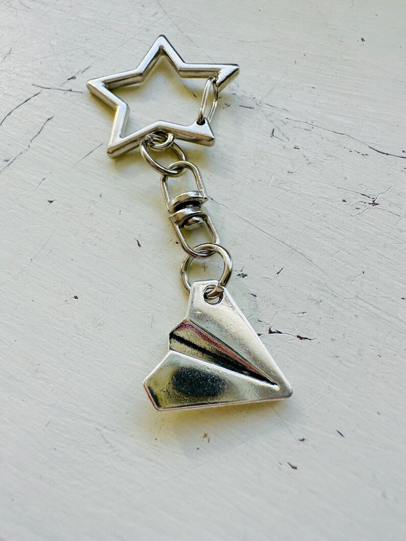 May include: Silver keychain with a star-shaped charm and a paper airplane charm.