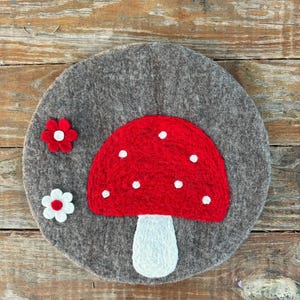 May include: A round felt coaster with a red and white mushroom design and two white flowers with red centers.