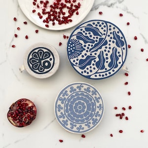 May include: Three reusable food wraps with blue and white floral patterns. The wraps are made of fabric and are designed to cover bowls and plates to keep food fresh.
