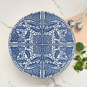 May include: A round, blue and white decorative serving tray with a floral design. The tray is divided into four sections, each with a symmetrical pattern of leaves and dots. The tray is on a white marble surface.