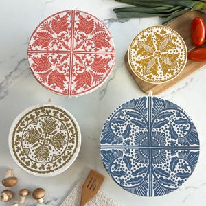 May include: Four reusable food covers with different patterned designs. The covers are made of fabric and have a white background with colorful patterns. The patterns include red and white floral designs, yellow and white geometric designs, and blue and white floral designs.