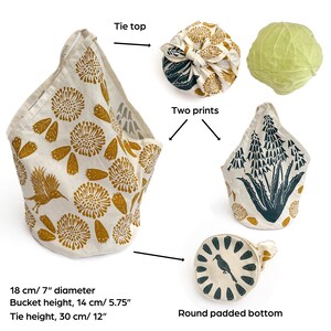 May include: A reusable fabric shopping bag with a round padded bottom and a tie top. The bag is made of natural fabric with a floral print in yellow and white. The bag is 7 inches in diameter and 5.75 inches tall. The tie is 12 inches long.