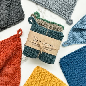 May include: A selection of knitted multi-cloths in shades of orange, yellow, blue, and grey. Each square cloth has a loop for hanging. A bundle of cloths is wrapped with a label that reads "MULTI-CLOTH".