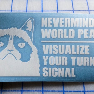 May include: White vinyl sticker with a grumpy cat face and the text "Nevermind world peace - Visualize your turn signal".