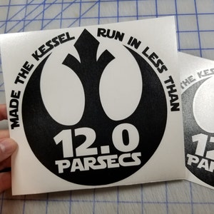 May include: Black and white sticker with the Rebel Alliance symbol. The text reads "Made the Kessel Run in less than 12.0 parsecs".