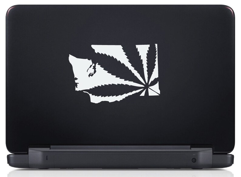 May include: A white vinyl sticker of a marijuana leaf superimposed over the outline of the state of Washington. The sticker is on a black laptop.
