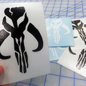 May include: A set of four Mandalorian symbol decals. The decals are black and white and feature the Mandalorian symbol. The decals are on a white background.